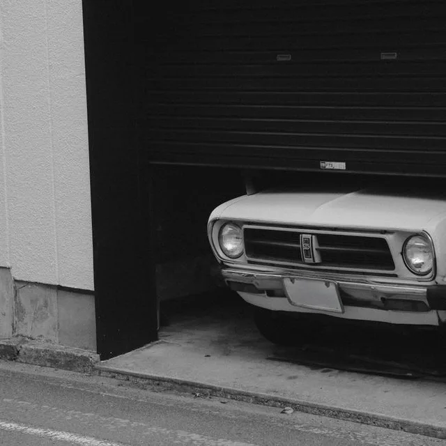 Une photo en noir et blanc montrant une voiture ancienne partiellement dissimulée sous une porte de garage.