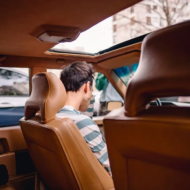 Vue de dos d'un homme assis à l'intérieur d'une voiture avec un toit ouvrant, vue depuis le siège arrière.