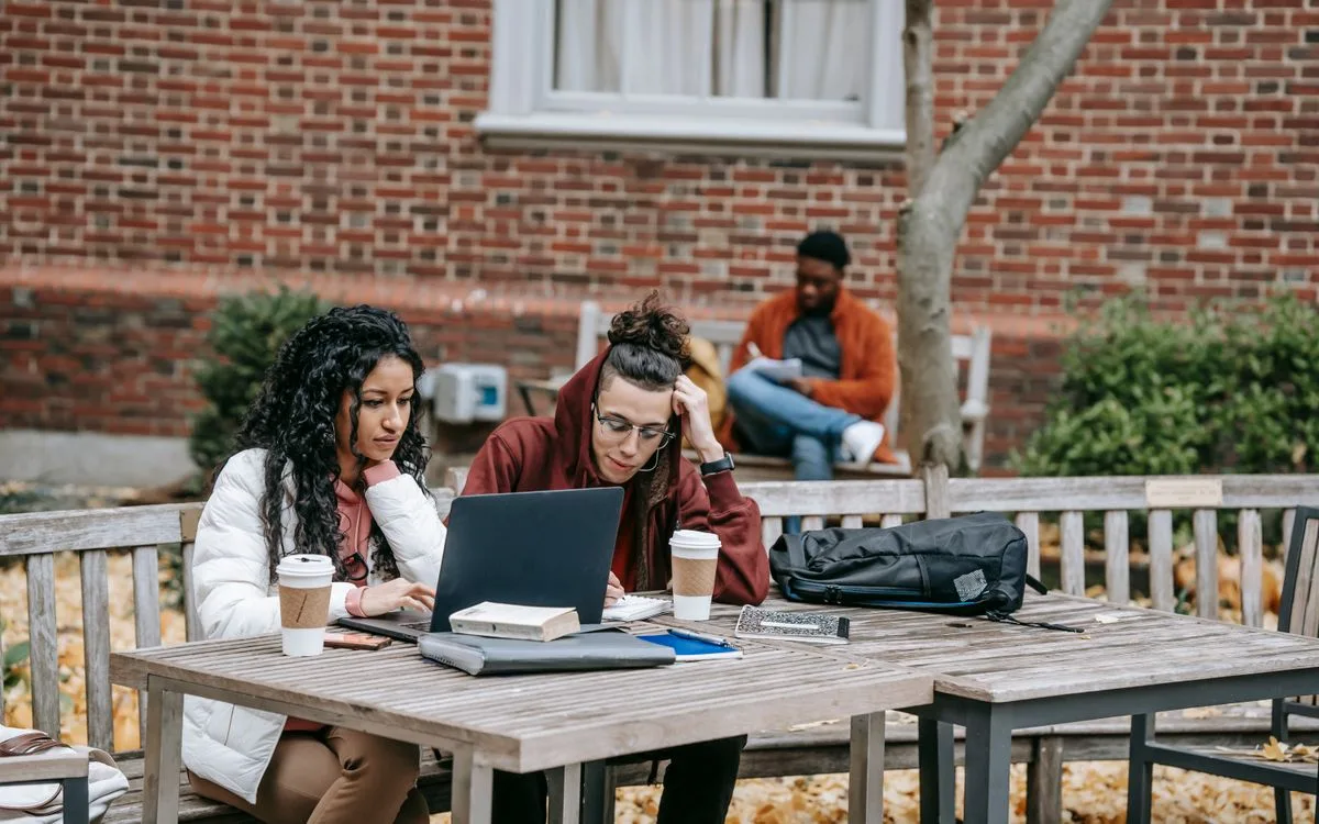 Deux étudiants penchés sur un ordinateur portable à une table de jardin, en automne